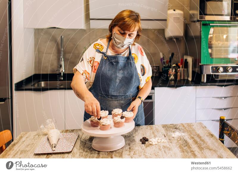 Female baker wearing mask decorating cupcakes on cakestand in workshop color image colour image indoors indoor shot indoor shots interior interior view