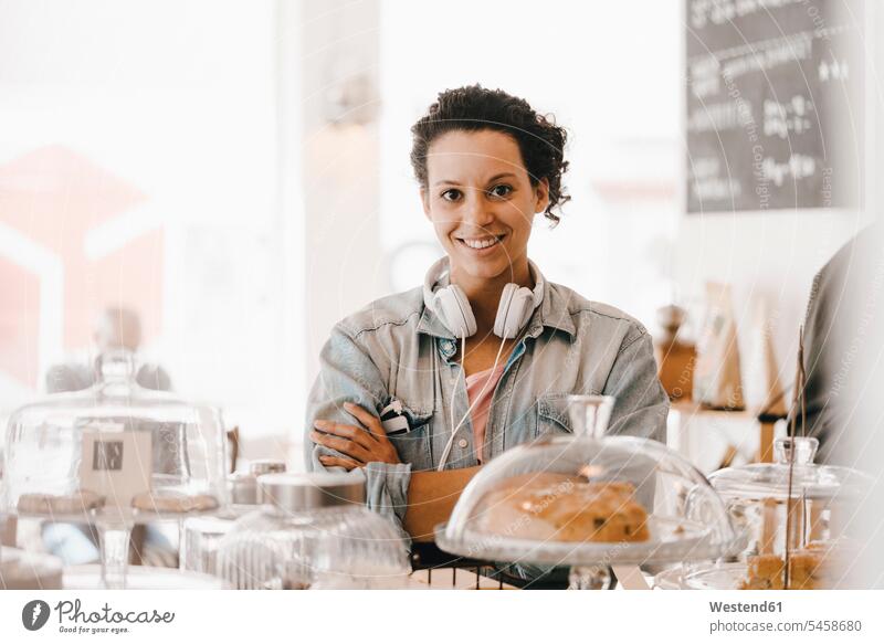 Woman with headphones standing in coffee shop with arms crossed cake pies cakes working At Work woman females women headset cafe smiling smile Sweet Food sweet
