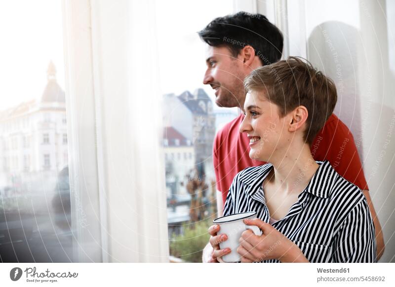 Relaxed couple standing at the window, woman drinking coffee Coffee relaxed relaxation happiness happy windows twosomes partnership couples Drink beverages