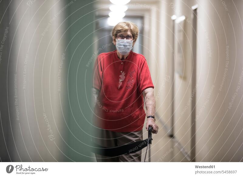 Senior woman wearing mask and walking with wheeled walker in corridor of retirement home Eye Glasses Eyeglasses specs spectacles go going stand at home hygienic