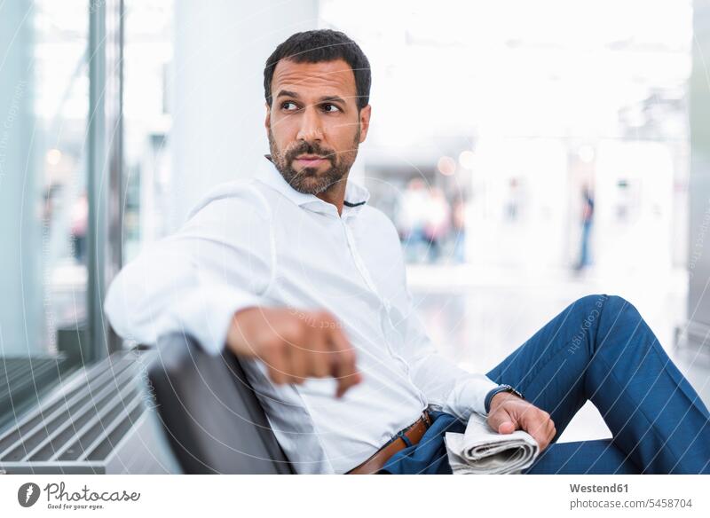 Businessman with a newspaper in waiting hall newspapers men males reading looking around looking round look round look around Business man Businessmen