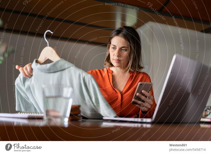 Businesswoman with smart phone looking at clothes while sitting at home color image colour image indoors indoor shot indoor shots interior interior view