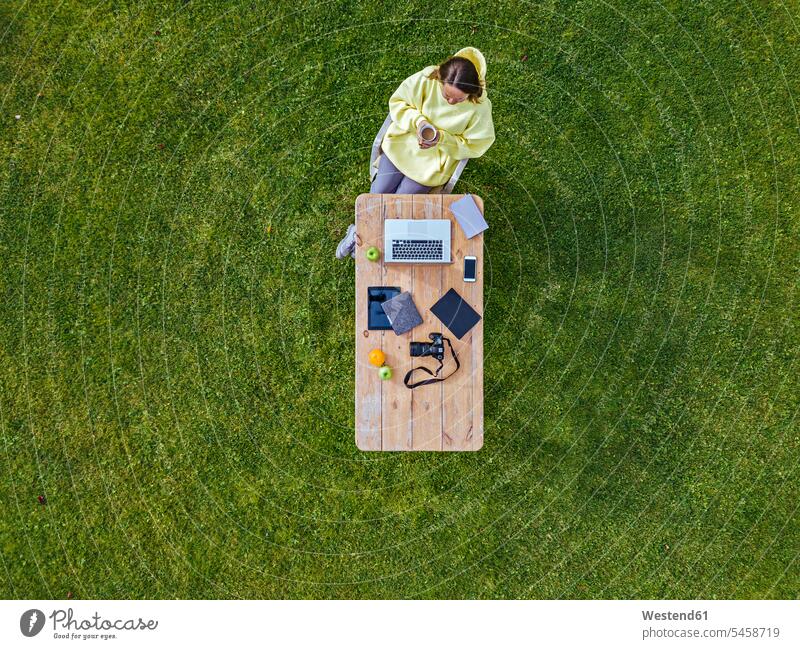 Aerial view of woman sitting at coffee table set on green lawn with mug of coffee in hands outdoors location shots outdoor shot outdoor shots day daylight shot