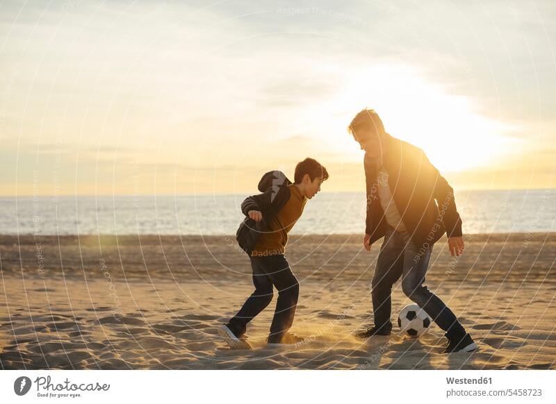 Father and son playing football on the beach at sunset father pa fathers daddy dads papa beaches sons manchild manchildren soccer ball soccer balls footballs