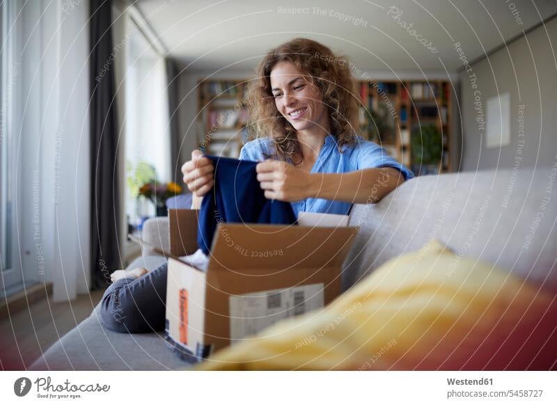 Smiling woman removing cloth from package while sitting on sofa at home color image colour image indoors indoor shot indoor shots interior interior view