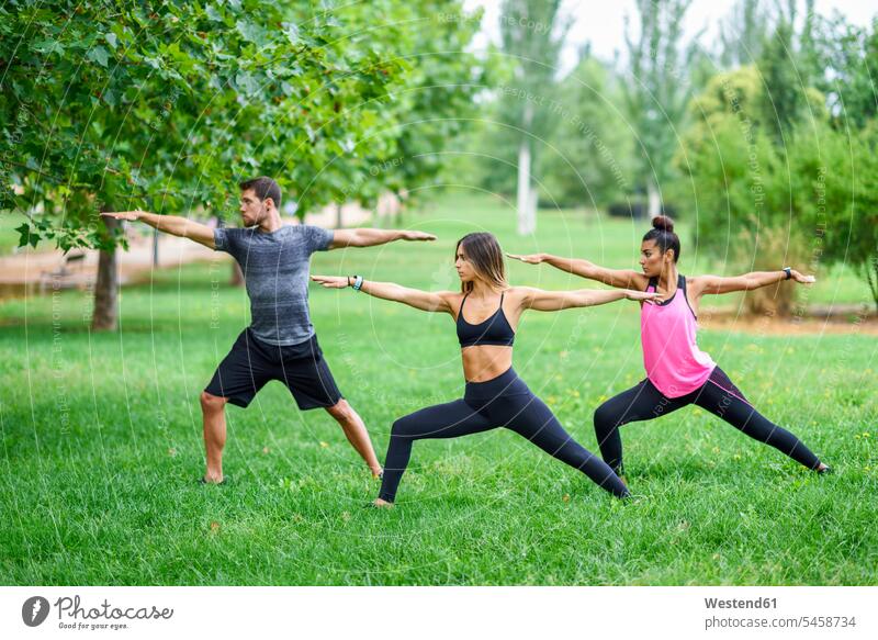Young people exercising yoga in a park exercise training practising stretching Warrior Pose Warrior Position Virabhadrasana parks Yoga Fitness fit practicing