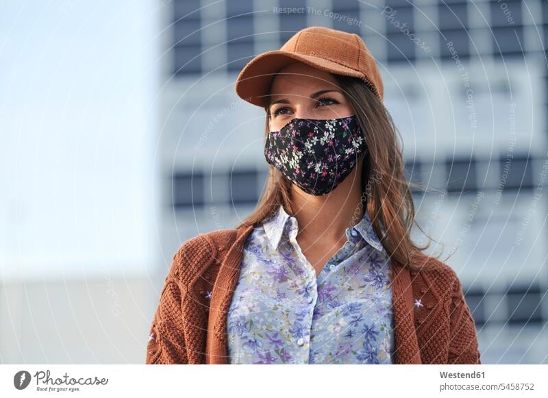 Young woman wearing cap and face mask looking away while standing in city color image colour image outdoors location shots outdoor shot outdoor shots day