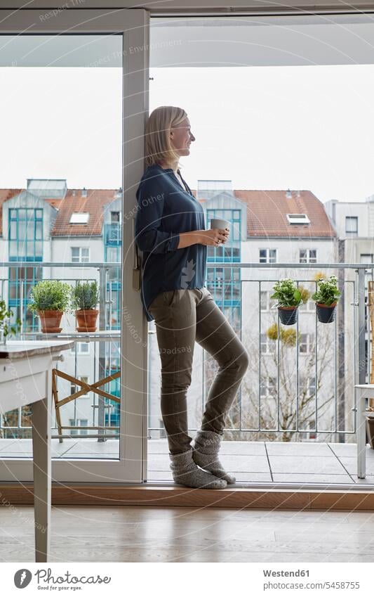Smiling woman holding cup of coffee looking out of balcony door Coffee balconies smiling smile balcony doors females women Drink beverages Drinks Beverage