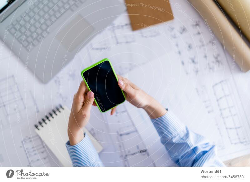 Close-up of woman in office using cell phone with blueprint on table human human being human beings humans person persons caucasian appearance
