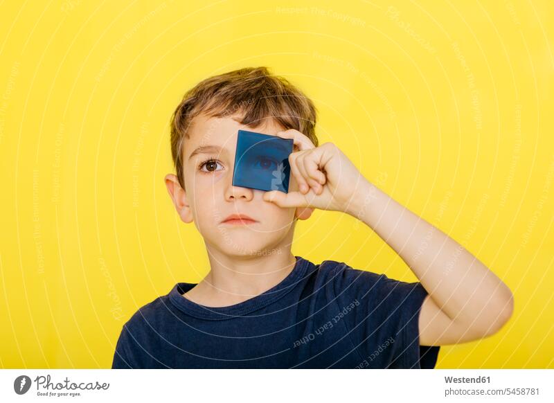 Close-up of cute boy holding blue acrylic glass against yellow background color image colour image coloured background colored background studio shot