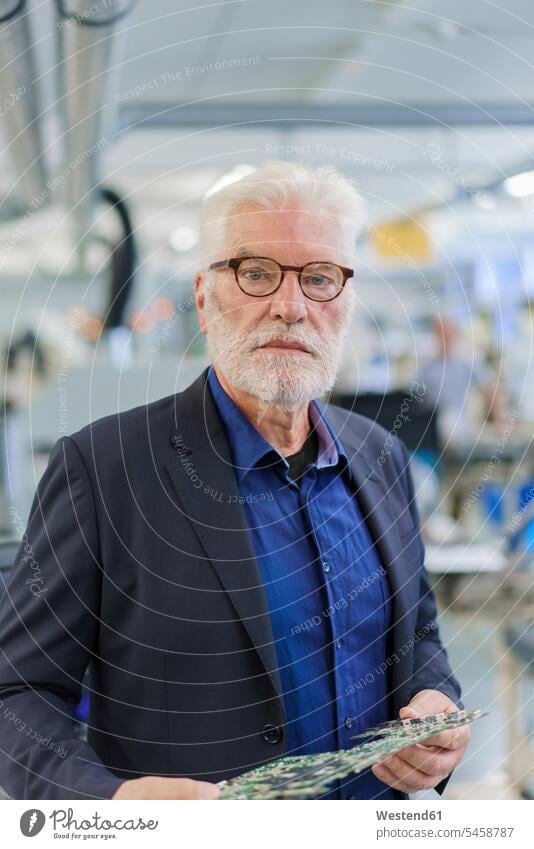 Confident senior male manager holding machine part while standing at factory color image colour image indoors indoor shot indoor shots interior interior view