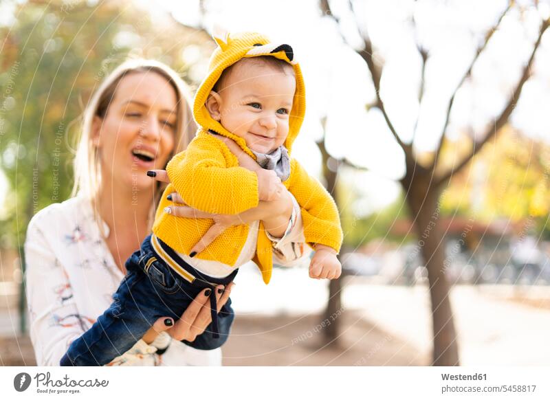Happy mother playing with baby boy in a park coat coats jackets hold smile delight enjoyment Pleasant pleasure Cheerfulness exhilaration gaiety gay glad Joyous