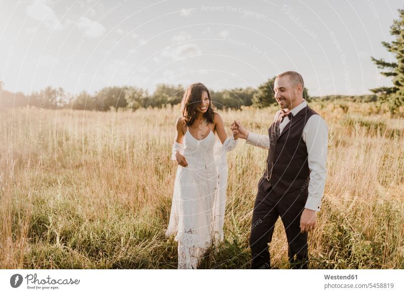 Couple holding hand and walking in field on sunny day color image colour image outdoors location shots outdoor shot outdoor shots daylight shot daylight shots