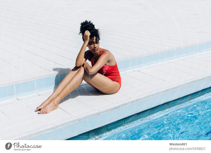 Portrait of pensive young woman wearing red swimsuit sitting at poolside swim wear bathing costume bathing costumes bathing suit bathing suits Swimming Costume
