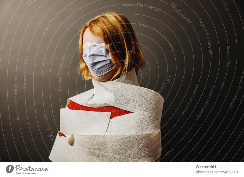 Teenage girl wrapped in toilet paper and face covered with protective face mask standing against gray background color image colour image day daylight shot