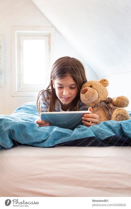 Portrait of smiling girl lying on bed with teddy bear using digital tablet Bed - Furniture beds teddies teddy bears teddy-bear relax relaxing smile play