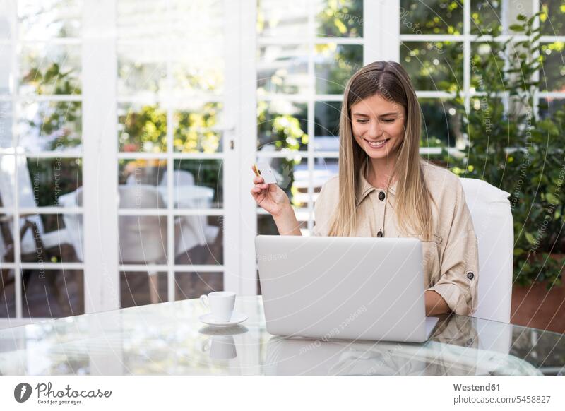 Happy young woman holding credit card while using laptop at table in coffee shop color image colour image indoors indoor shot indoor shots interior