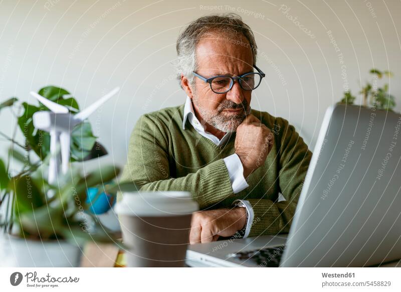 Man wearing eyeglasses using laptop while sitting by table at home color image colour image indoors indoor shot indoor shots interior interior view Interiors