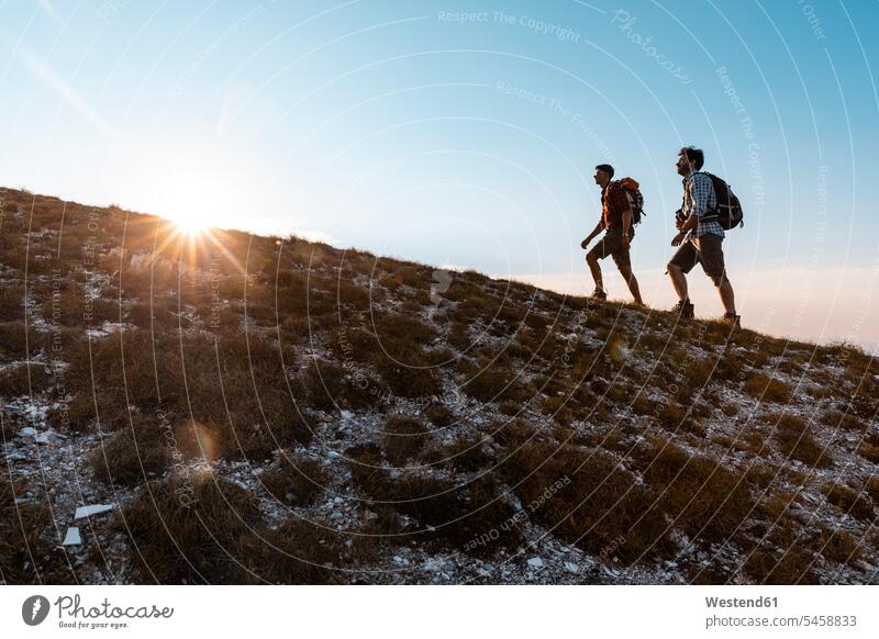 Italy, Monte Nerone, two men hiking in mountains at sunset hike man males sunsets sundown mountain range mountain ranges hiker wanderers hikers walking going