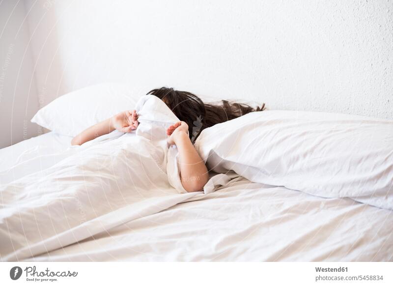 Girl lying in bed covering her face with blanket sleeping asleep girl females girls duvets blankets child children kid kids people persons human being humans