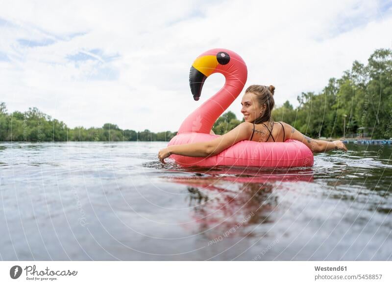 Young woman floating on a lake in a pink flamingo floating tire swim wear bikinis floating tires floating tyre floating tyres relax relaxing smile summer time