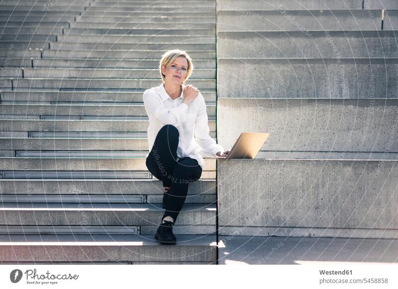 Young busineswoman sitting on stairs, using laptop stairway using a laptop Using Laptops career Seated Laptop Computers laptops notebook businesswoman