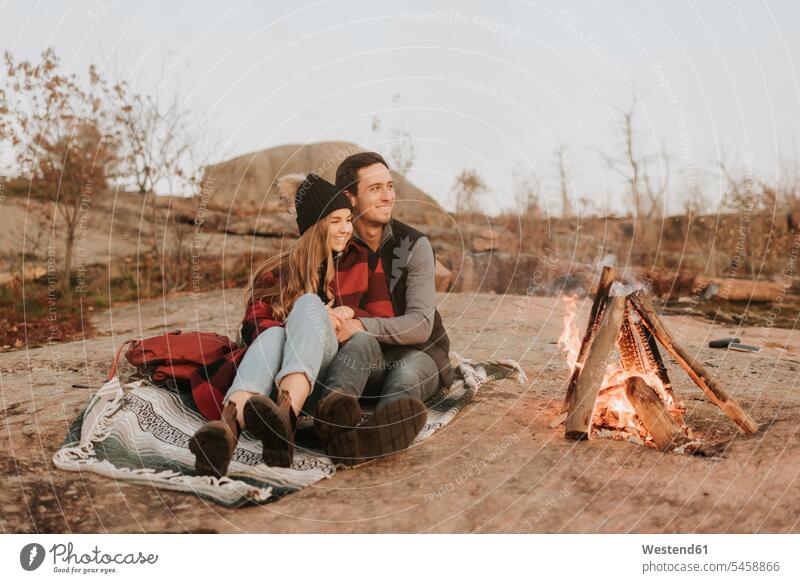 Young couple sitting together in front of campfire outdoors location shots outdoor shot outdoor shots day daylight shot daylight shots day shots daytime