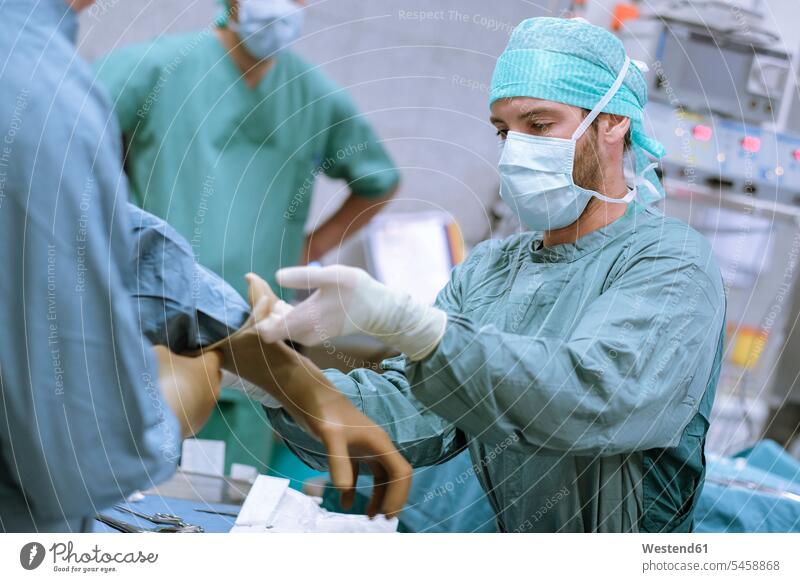 Assistant helping surgeon putting on glove before an operation surgery surgeries operating surgical gown scrubs Operating Gown assistance assisting Help