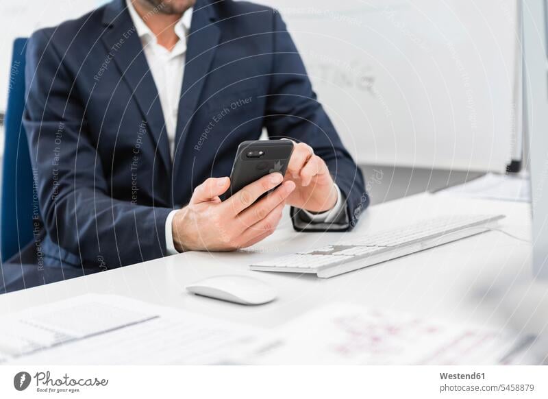 Close-up of businessman sitting at desk in office using cell phone mobile phone mobiles mobile phones Cellphone cell phones offices office room office rooms