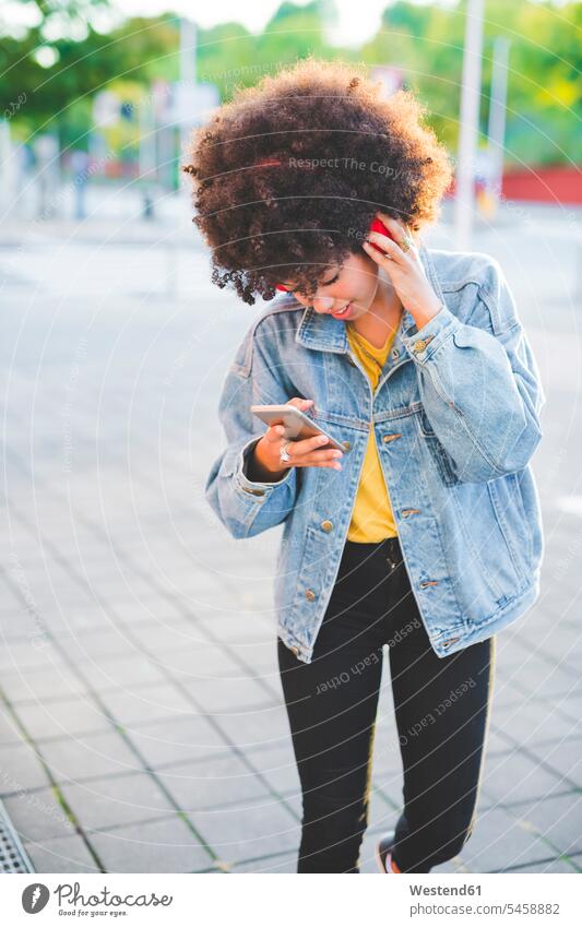 Young woman with afro hairdo using smartphone and headphones in the city human human being human beings humans person persons curl curled curls curly hair