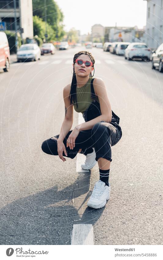 Portrait of a confident stylish young woman crouching on the street in the city Eye Glasses Eyeglasses specs spectacles Pair Of Sunglasses sun glasses Distinct