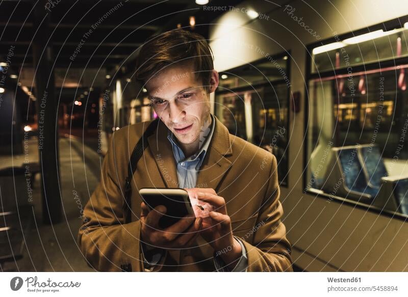 Businessman using cell phone at tram station at night by night nite night photography tram stop tram stops tram stations mobile phone mobiles mobile phones