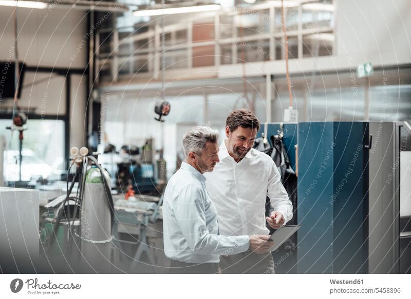 Businessman discussing with male colleague over digital tablet in industry color image colour image Germany indoors indoor shot indoor shots interior