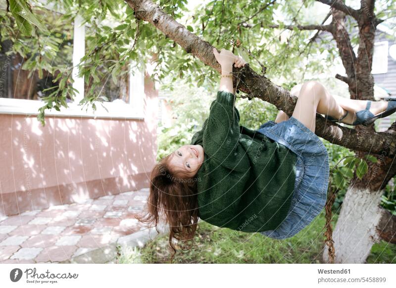 Cute girl hanging from tree branch in back yard color image colour image outdoors location shots outdoor shot outdoor shots day daylight shot daylight shots
