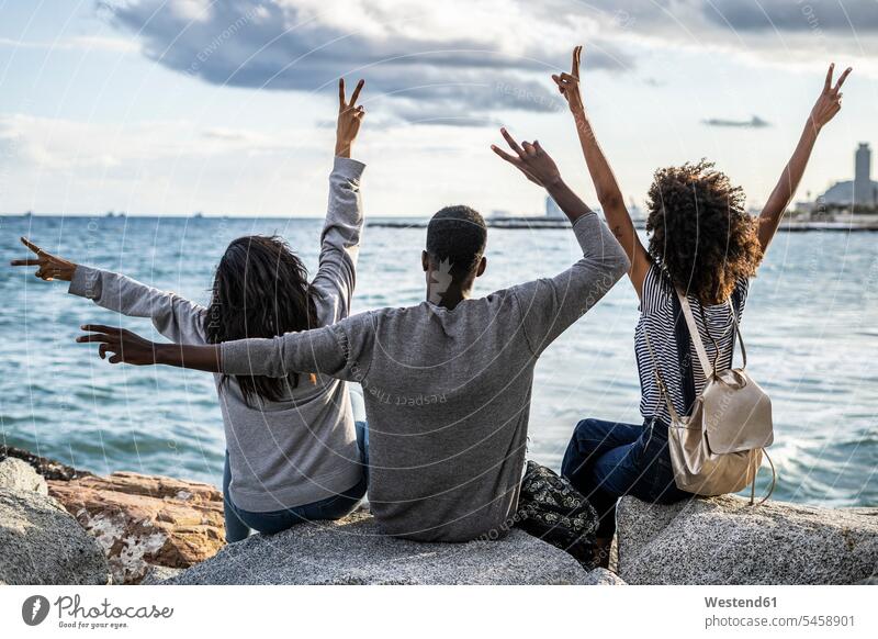 Three friends sitting on the beach, lookin at the sea, cheering, rear view Peace peacefulness Enjoyment Amusement pleasure enjoy enjoying Freedom Liberty free