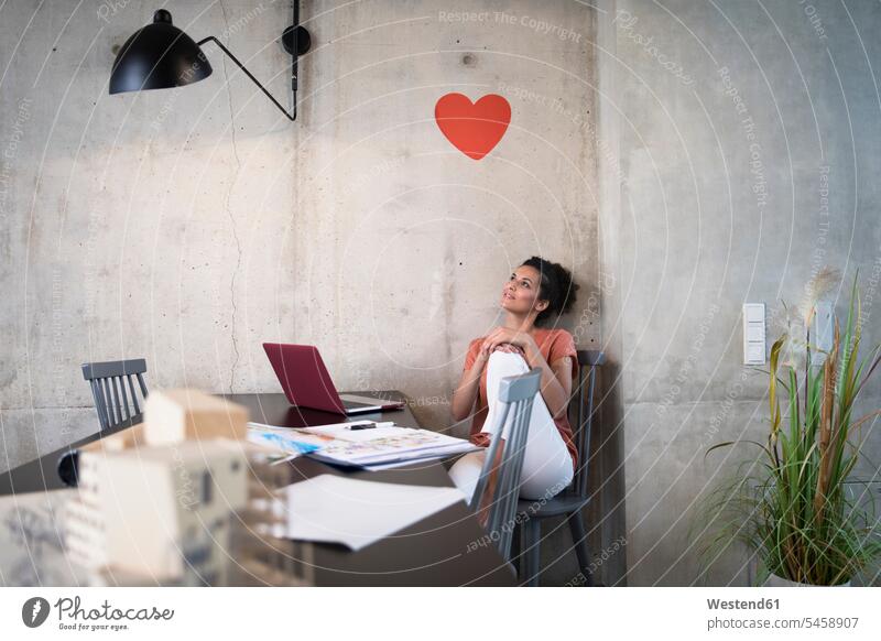 Businesswoman sitting at table in a loft under a heart on concrete wall lofts hearts heart shapes Seated businesswoman businesswomen business woman