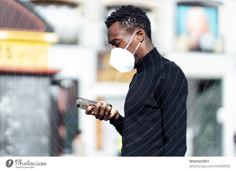 Young man wearing face mask using mobile phone while standing outdoors color image colour image location shots outdoor shot outdoor shots day daylight shot