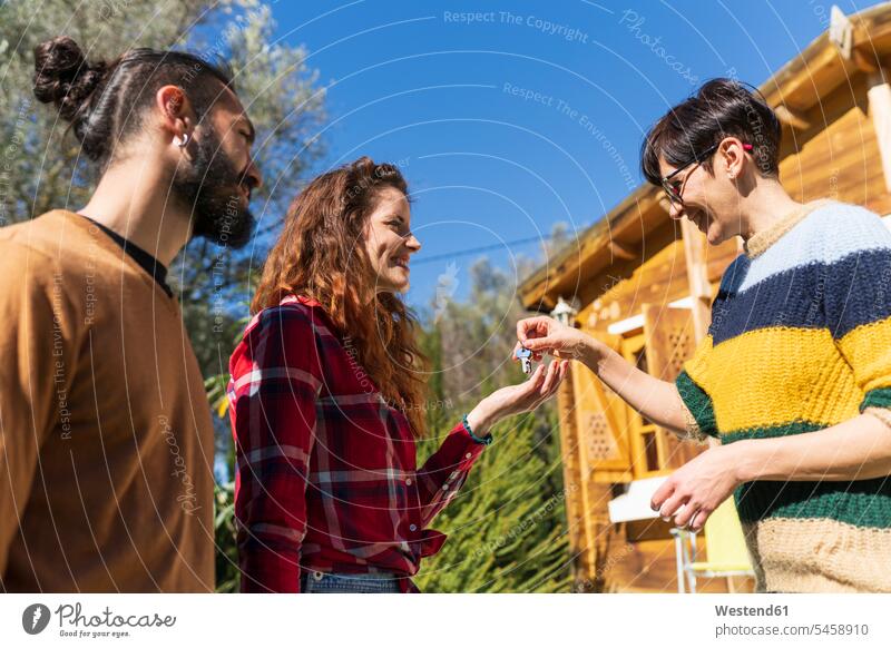 Host welcoming young couple outside a cabin in the countryside handing over house key touristic tourists keys Eye Glasses Eyeglasses specs spectacles greet give