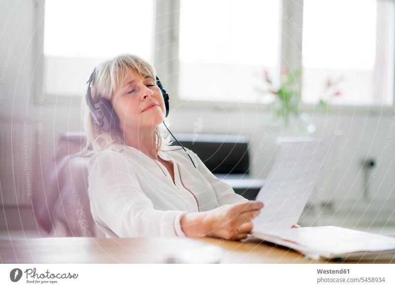 Relaxed mature businesswoman wearing headphones at desk desks businesswomen business woman business women relaxed relaxation headset Table Tables