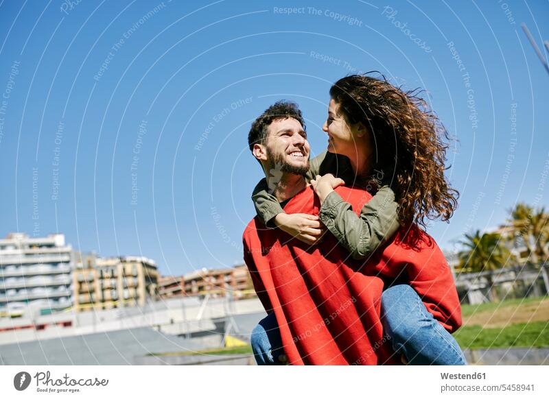 Happy young man giving girlfriend a piggyback ride couple twosomes partnership couples piggy-back pickaback Piggybacking Piggy Back happiness happy people
