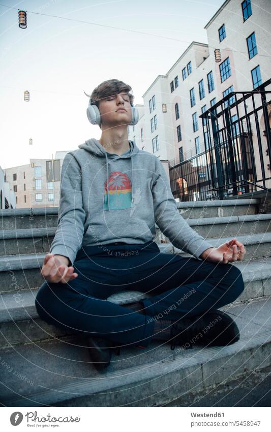 Teenager sitting on steps meditating in the city and listening to music headphone headset relax relaxing hear smile Seated happy Contented Emotion pleased