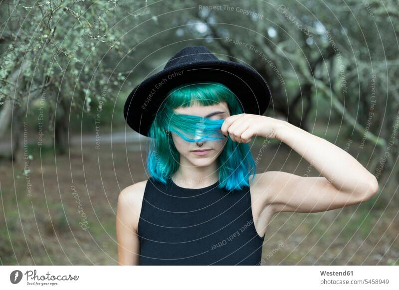 Portrait of young woman with dyed blue and green hair wearing black hat on rainy day hats jewelry colour colours wetness country countryside Individuality