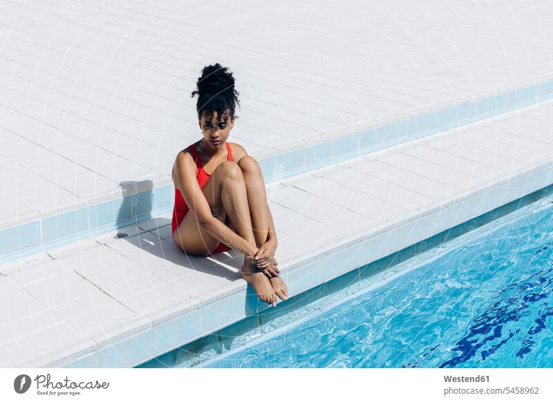 Pensive young woman wearing red swimsuit sitting at poolside tiles swim wear bathing costume bathing costumes bathing suit bathing suits Swimming Costume