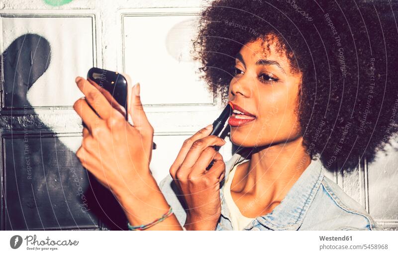 Close-up of woman with curly hair applying lipstick while looking in mirror at night color image colour image Spain leisure activity leisure activities