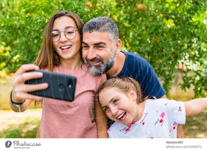 Happy father with two daughters taking selfie in garden T- Shirt t-shirts tee-shirt telecommunication phones telephone telephones cell phone cell phones