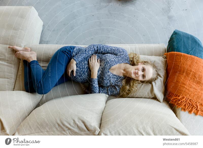 Portrait of smiling pregnant woman lying on couch at home laying down lie lying down smile portrait portraits females women Pregnant Woman settee sofa sofas