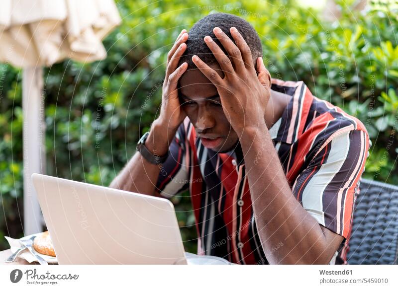 Tensed young man sitting with head in hands while looking at laptop in cafe color image colour image day daylight shot daylight shots day shots daytime Spain