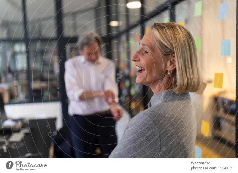 Happy businesswoman with colleague and sticky notes at glass pane in office Occupation Work job jobs profession professional occupation business life