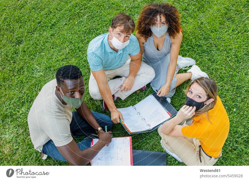Students wearing protective mask studying while sitting together on grass in university campus color image colour image day daylight shot daylight shots