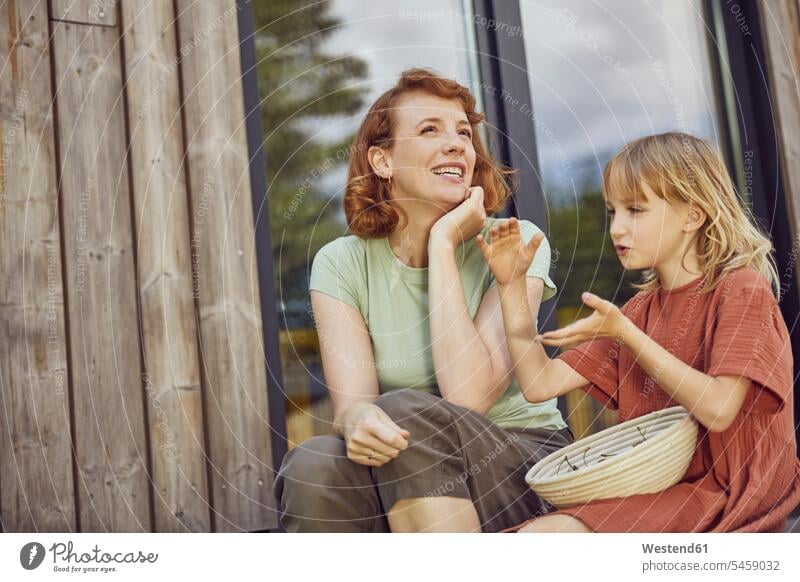 Smiling mother talking with daughter while sitting outside tiny house color image colour image Germany leisure activity leisure activities free time